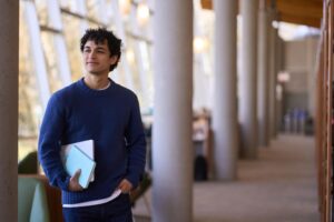 Studente con galf blu che cammina in un corridoio con colonnato sulla sinistra dell'immagine
