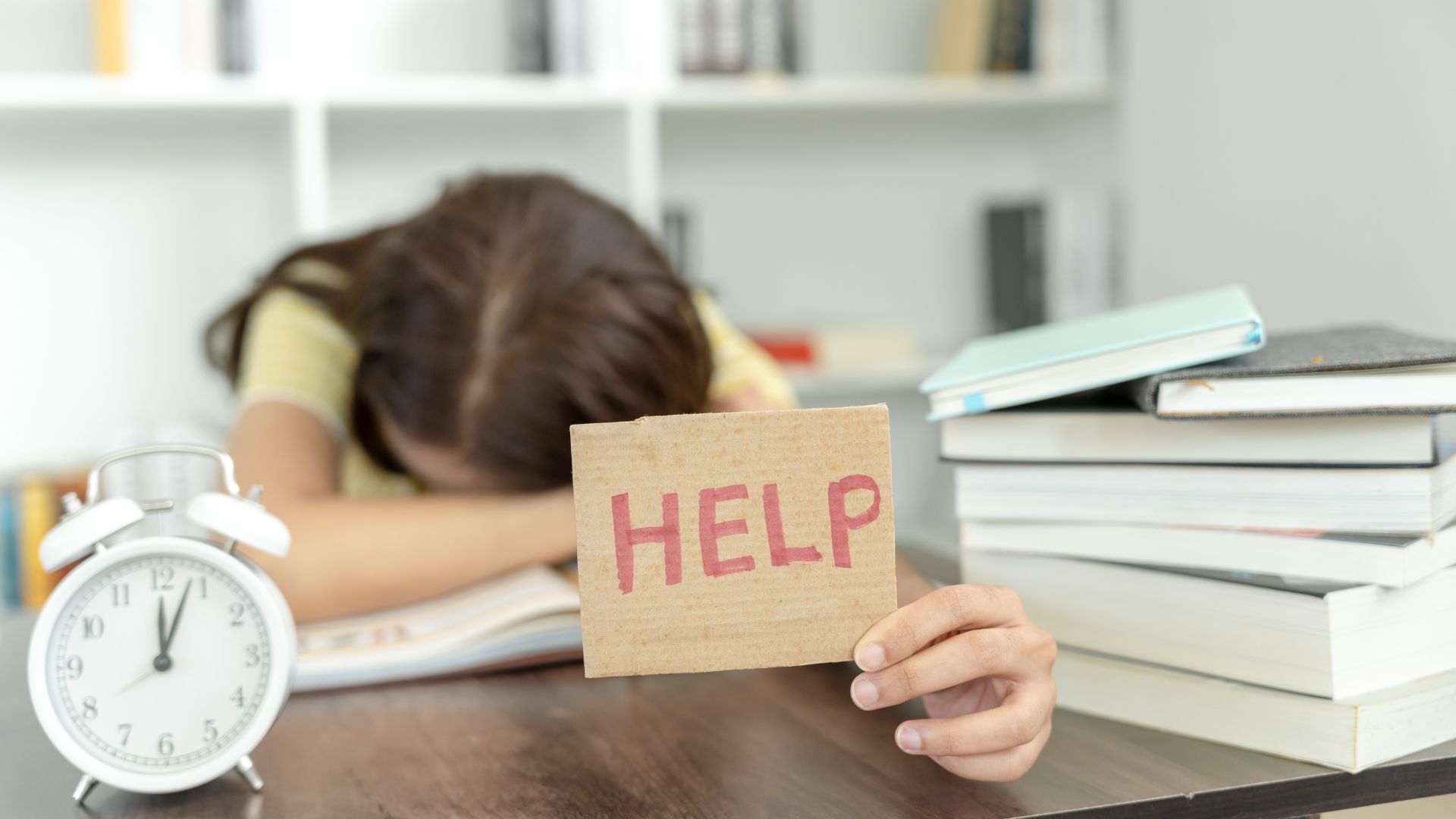 Ragazza che studia ed alza un cartello con scritto "help"