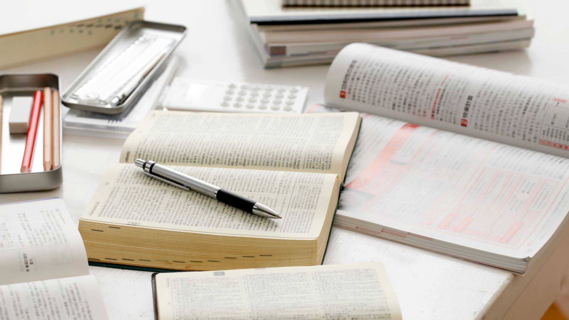 Dizionario, libri e penne sopra un banco